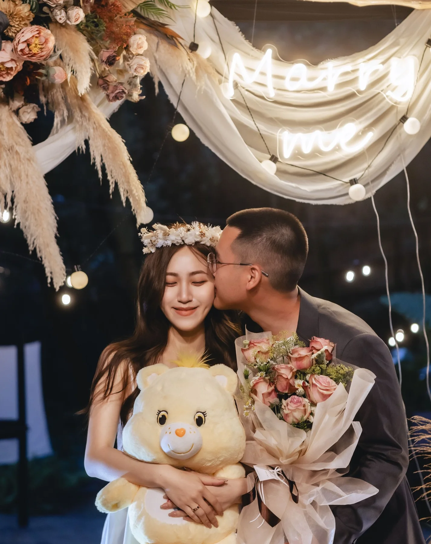抱著熊與花,在「Marry me」燈字下
