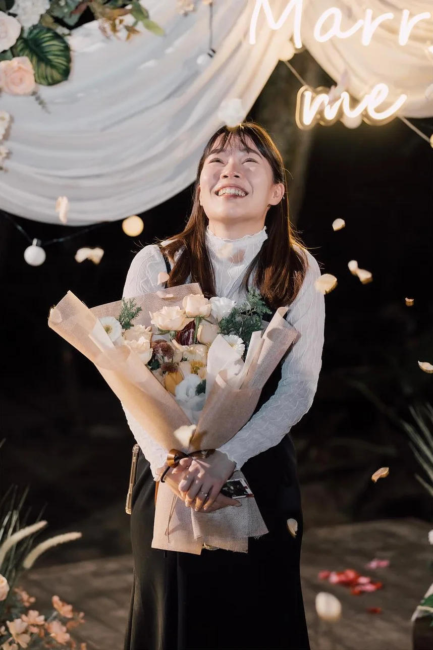 「Marry me」燈字下,她抱著花