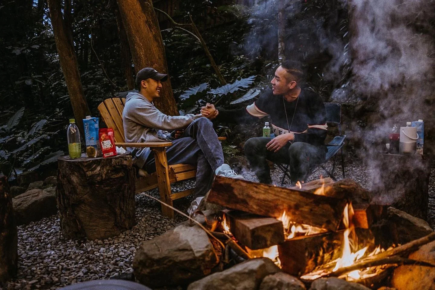 兩位朋友坐在營火旁聊天,煙在林間散開
